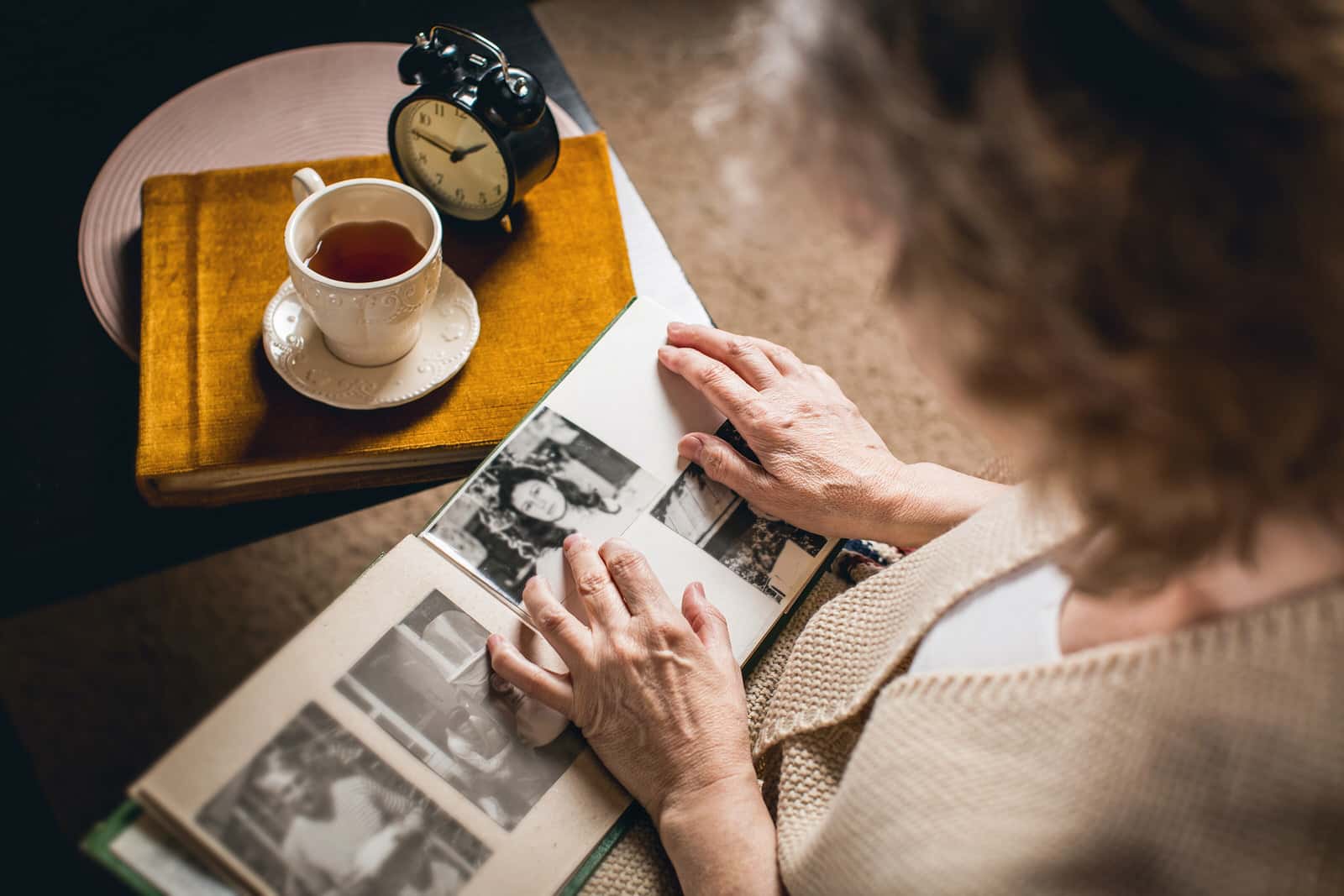 An older woman looks back on vintage photos while drinking coffee. Nostalgia marketing depends on these strong connections to the past.
