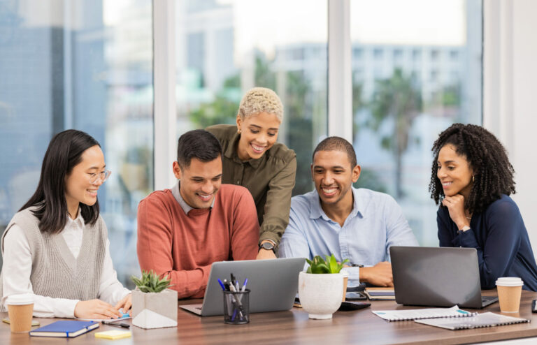 A group of five people sitting at a conference table, looking at a laptop.