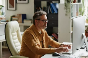 A middle aged man sits at a home computer.